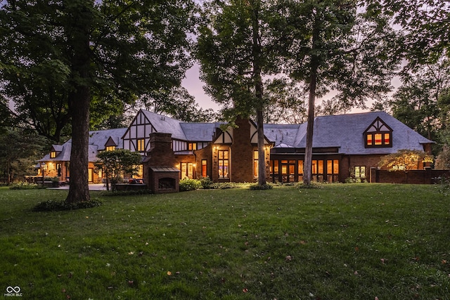 back of house at dusk with a lawn and brick siding
