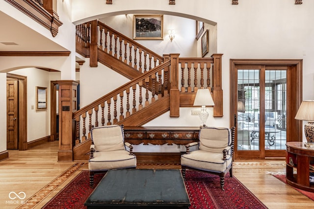 stairway featuring wood finished floors, arched walkways, baseboards, and a high ceiling