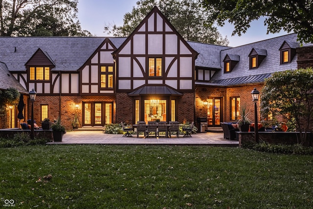 rear view of property with a lawn, brick siding, french doors, and stucco siding