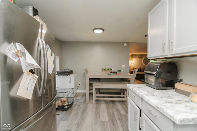 kitchen with white cabinetry, a toaster, light stone counters, freestanding refrigerator, and light wood-style flooring