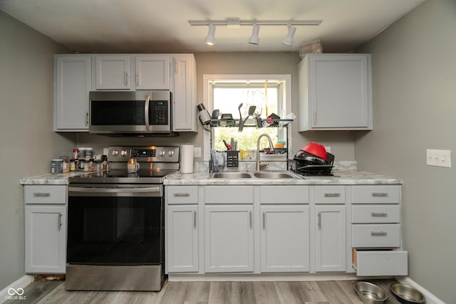 kitchen featuring light wood-style floors, baseboards, white cabinets, a sink, and stainless steel appliances