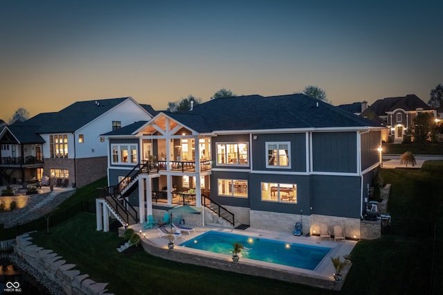 back of property at dusk with stairway, a lawn, an outdoor pool, and a patio area