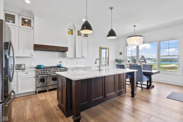 kitchen with light stone counters, appliances with stainless steel finishes, a sink, decorative backsplash, and light wood-type flooring