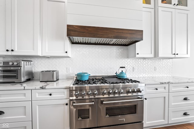 kitchen featuring backsplash, double oven range, a toaster, light stone counters, and white cabinetry