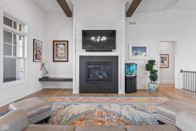 living room featuring a large fireplace, wood finished floors, beam ceiling, and visible vents