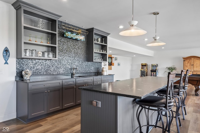 bar with indoor wet bar, a sink, light wood finished floors, and backsplash