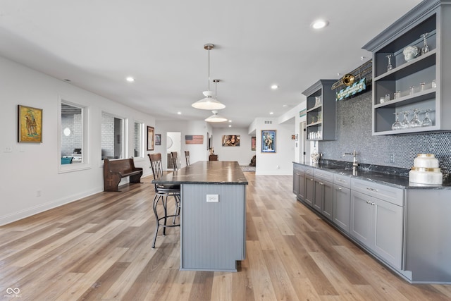 kitchen featuring gray cabinets, a kitchen island, backsplash, open shelves, and a breakfast bar