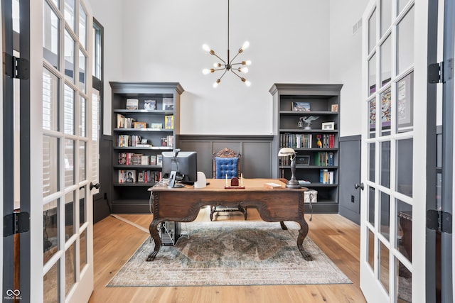 office with french doors, an inviting chandelier, a high ceiling, and wood finished floors