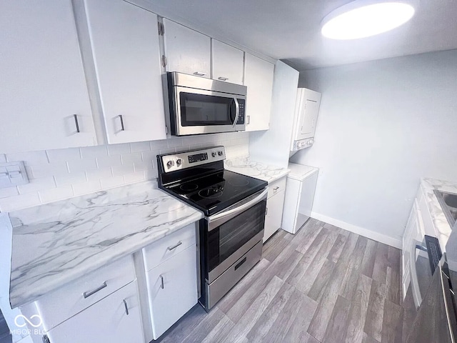 kitchen featuring stacked washer / drying machine, light wood-style floors, appliances with stainless steel finishes, backsplash, and white cabinetry