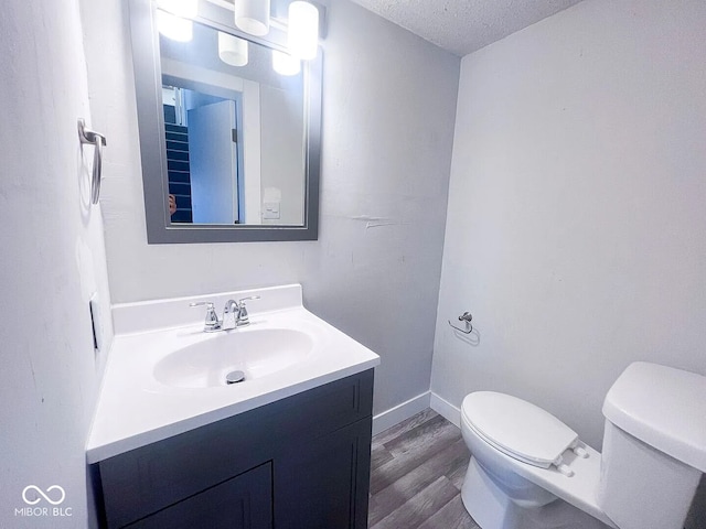 bathroom with wood finished floors, toilet, vanity, baseboards, and a textured ceiling