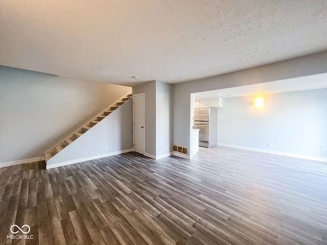 unfurnished living room featuring baseboards, stairway, wood finished floors, and a textured ceiling