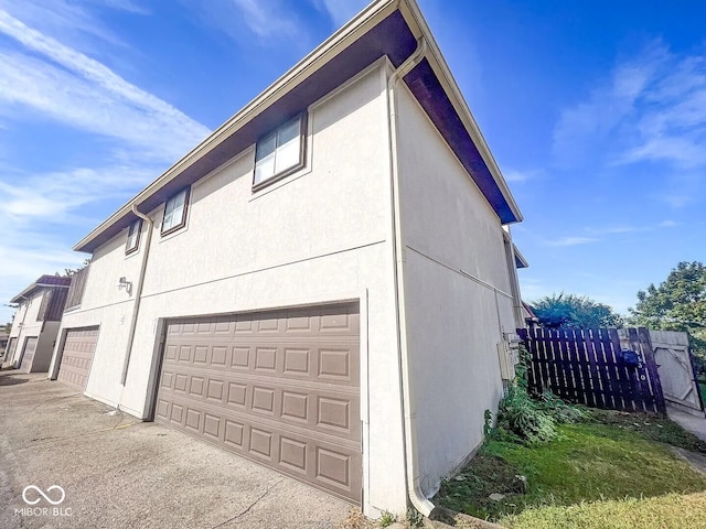 view of side of property with stucco siding, fence, and an attached garage