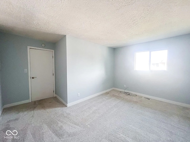 carpeted spare room with a textured ceiling, visible vents, and baseboards