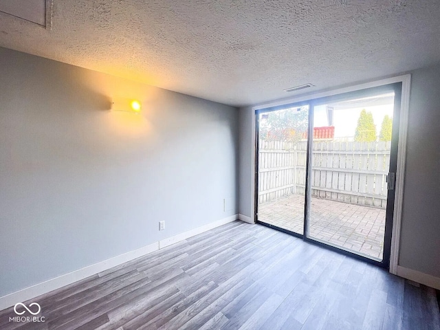 spare room with a textured ceiling, visible vents, wood finished floors, and baseboards