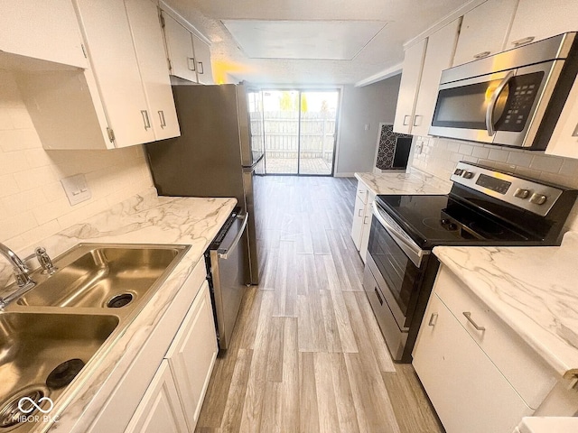 kitchen with a sink, tasteful backsplash, light wood-type flooring, white cabinetry, and appliances with stainless steel finishes