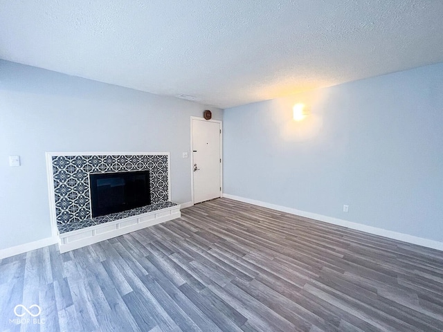 unfurnished living room with a fireplace, a textured ceiling, wood finished floors, and baseboards