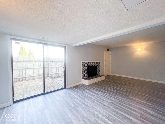 unfurnished living room featuring baseboards, wood finished floors, a textured ceiling, and a fireplace with raised hearth