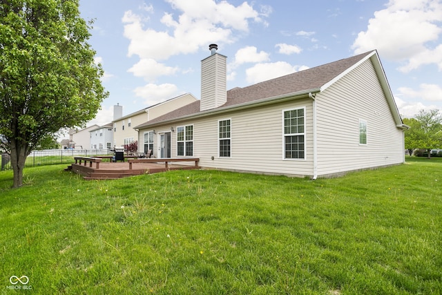 back of house with a lawn, a deck, fence, and a chimney