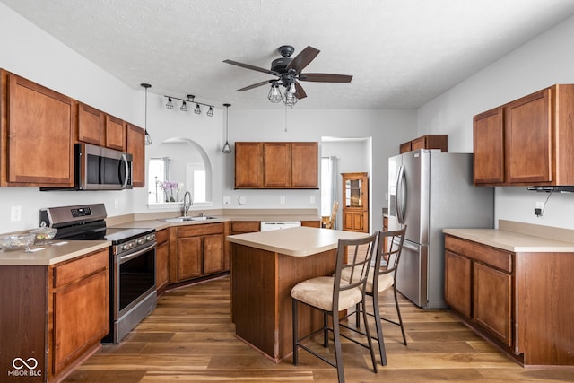 kitchen featuring ceiling fan, a kitchen island, a sink, light wood-style floors, and stainless steel appliances