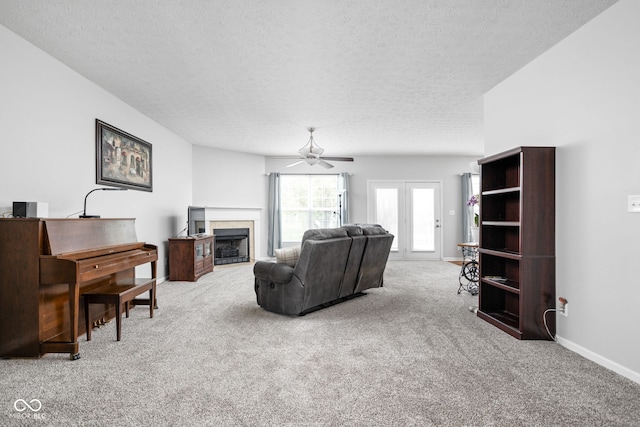 living room featuring a ceiling fan, a textured ceiling, a fireplace with flush hearth, baseboards, and carpet