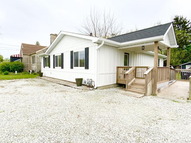 exterior space with board and batten siding, a chimney, covered porch, and roof with shingles