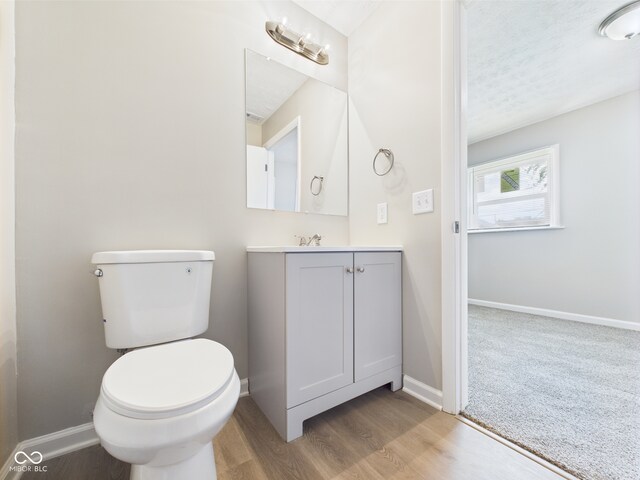 bathroom with baseboards, wood finished floors, toilet, and vanity
