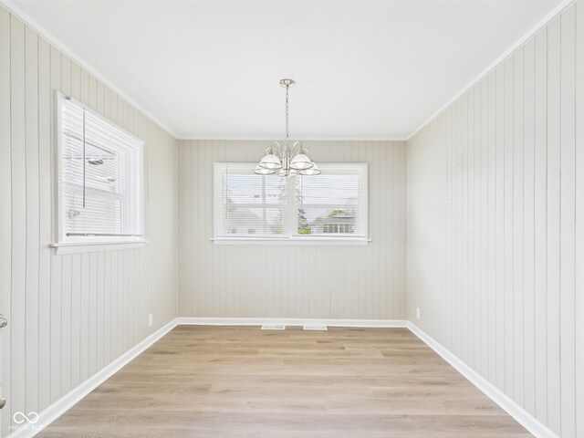 unfurnished dining area featuring an inviting chandelier, baseboards, crown molding, and light wood-style floors