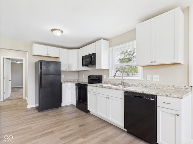 kitchen with a sink, light stone counters, black appliances, light wood finished floors, and white cabinetry