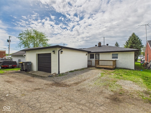 back of house with a chimney, a wooden deck, a garage, brick siding, and an outdoor structure
