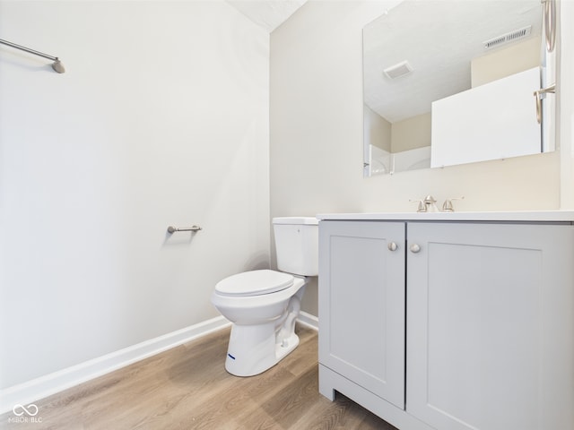 bathroom with vanity, toilet, baseboards, wood finished floors, and visible vents