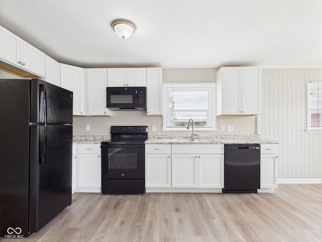 kitchen with white cabinets, a sink, black appliances, and light wood-style floors