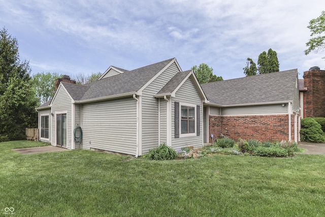 view of front facade with brick siding, a shingled roof, a front yard, and a chimney