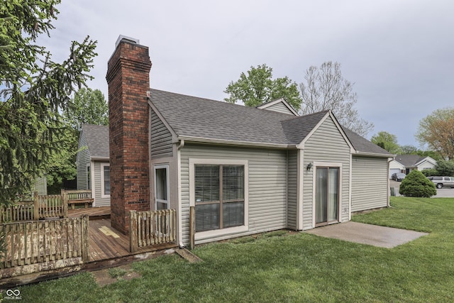 back of property with a lawn, a wooden deck, a chimney, and roof with shingles