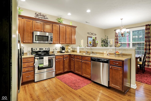 kitchen featuring a peninsula, light wood-type flooring, brown cabinets, a sink, and appliances with stainless steel finishes
