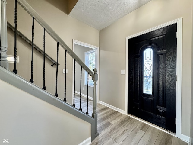 entrance foyer featuring stairway, light wood-style flooring, a textured ceiling, and baseboards