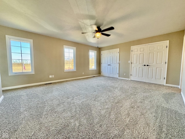 unfurnished bedroom with carpet floors, baseboards, a ceiling fan, and multiple closets