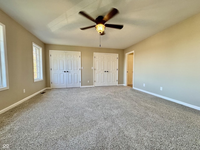 unfurnished bedroom with baseboards, carpet flooring, ceiling fan, visible vents, and two closets