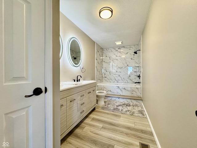 bathroom featuring toilet, wood finished floors, a combined bath / shower with marble appearance, a textured ceiling, and vanity
