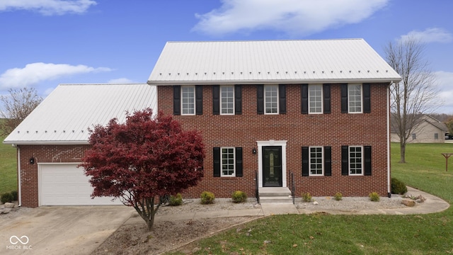 colonial home with concrete driveway, a front yard, metal roof, and an attached garage