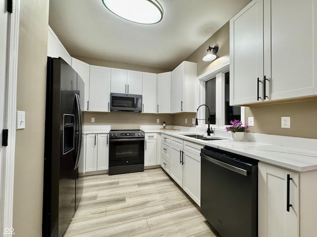 kitchen with a sink, stainless steel range with electric stovetop, dishwashing machine, black fridge, and white cabinetry