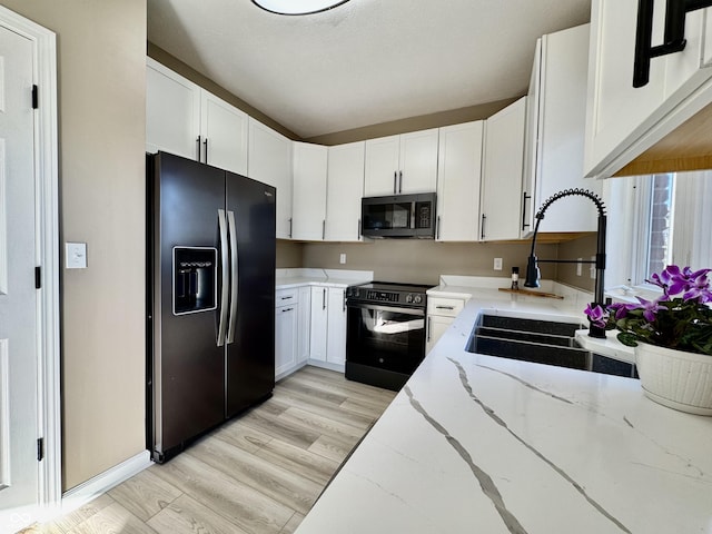 kitchen featuring light stone counters, a sink, black appliances, white cabinets, and light wood-type flooring