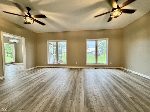 unfurnished living room featuring ceiling fan with notable chandelier, baseboards, and wood finished floors