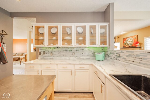 kitchen featuring glass insert cabinets, white cabinets, a sink, light wood-style flooring, and backsplash