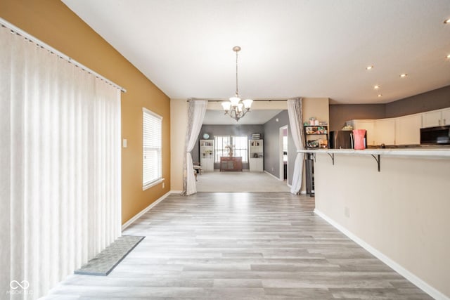 unfurnished dining area featuring baseboards, recessed lighting, light wood-style flooring, and a notable chandelier