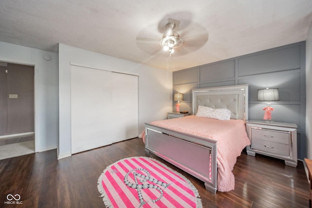 bedroom featuring ceiling fan, a decorative wall, baseboards, dark wood-style floors, and a closet
