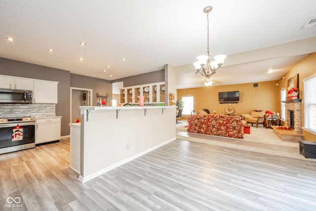 kitchen with appliances with stainless steel finishes, light wood-style floors, a breakfast bar area, white cabinetry, and open floor plan