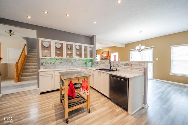 kitchen with backsplash, light wood-type flooring, dishwasher, a sink, and white cabinets
