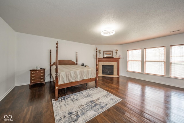 bedroom featuring a textured ceiling, baseboards, wood finished floors, a tile fireplace, and visible vents