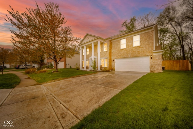 neoclassical home with driveway, a front yard, brick siding, fence, and an attached garage