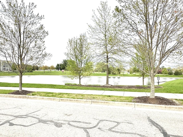 view of asphalt road featuring sidewalks, a water view, and curbs